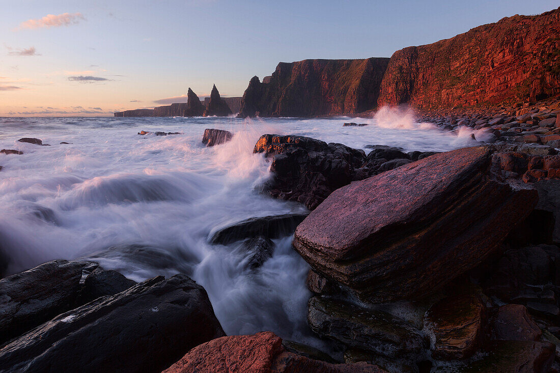 Impressively illuminated red, wild coast of Duncansby Head on the northeastern coast of Scotland with the Duncansby Stacks in the background, United Kingdom