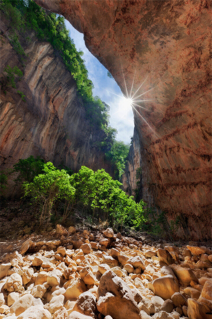 Blick aus der Cueva de la Ermita mit Sonnenstrahlen am Grund des tief eingeschnittenen Canyons Gargante Verde in Südspanien, Sierra de Grazalema, Andalusien, Spanien