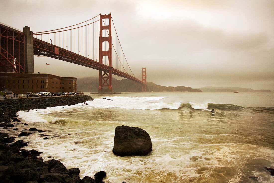 USA, California, San Francisco, the Golden Gate Bridge with a surfer on a wave in the foreground, Fort Point