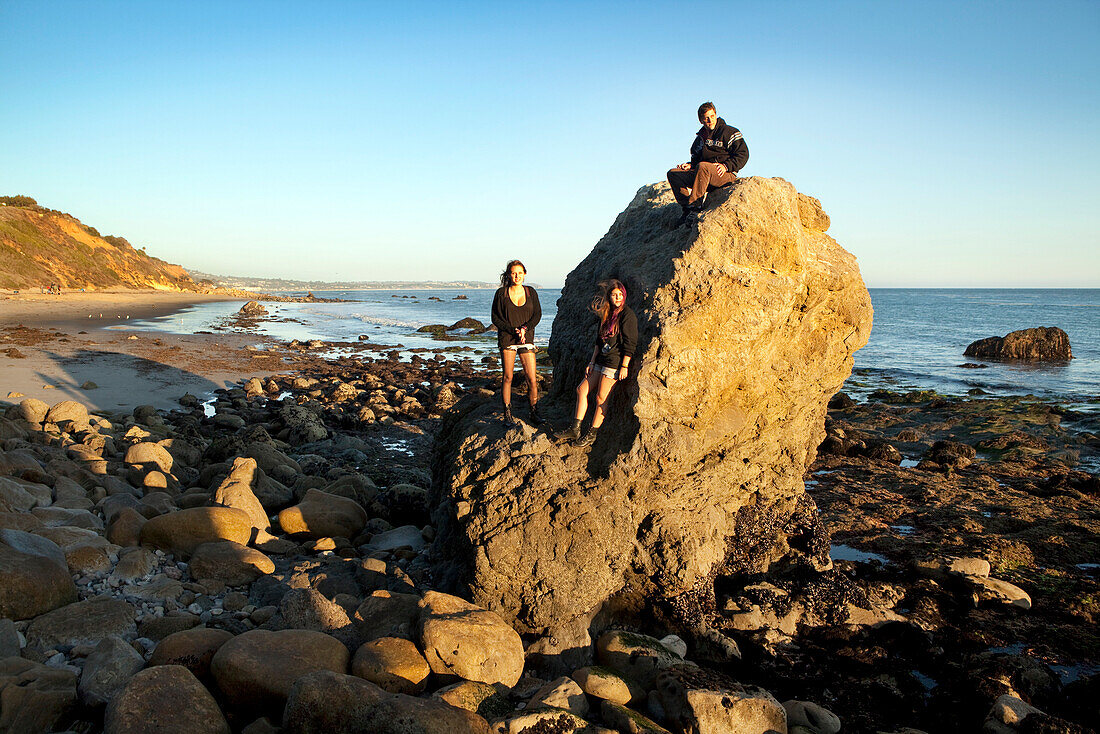 USA, California, Malibu, El Pescador Beach, friends Parker, Remi and April hang out on a large rock formation