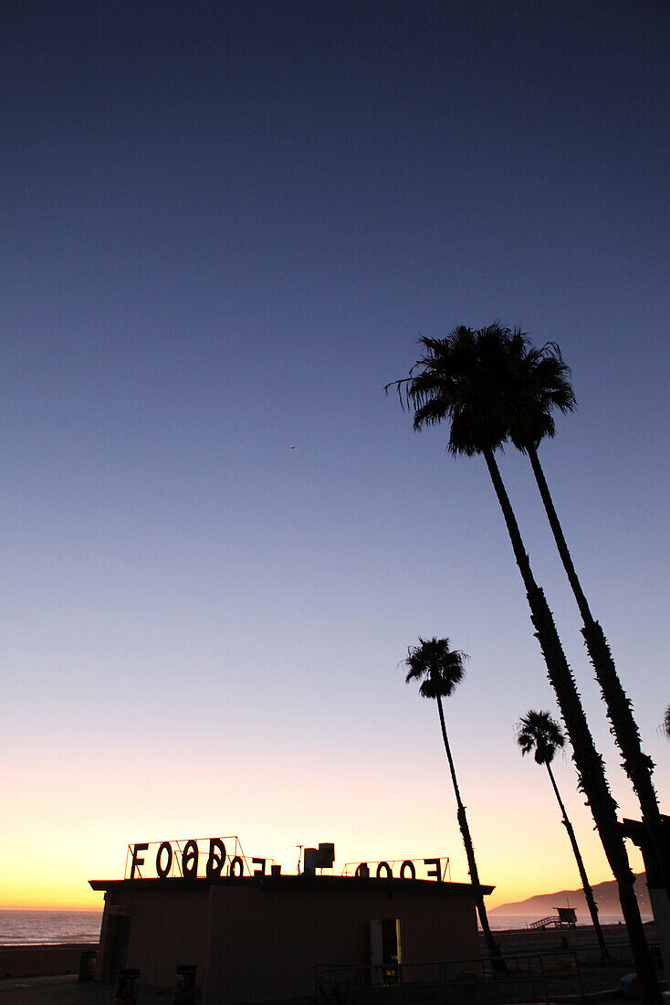 USA, California, Malibu, sunset silouette of a restaurant, palm trees and a lifeguard station at Zuma Beach