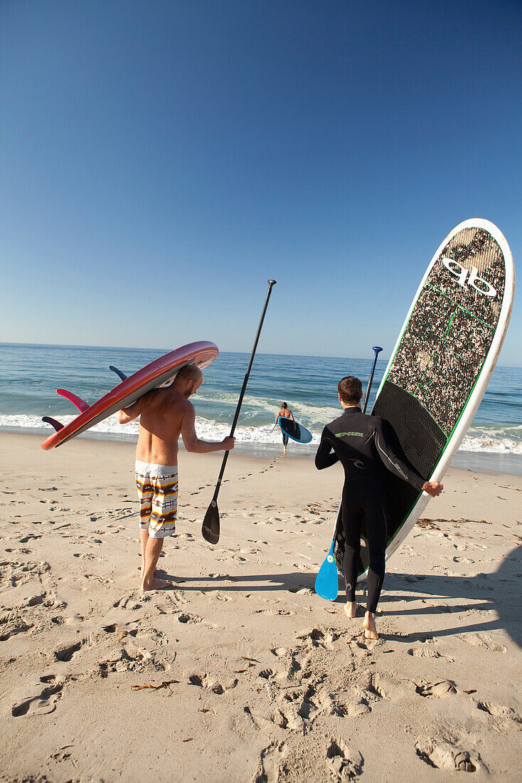 USA, California, Malibu, paddleboarders walk their boards down to the water at Zuma Beach