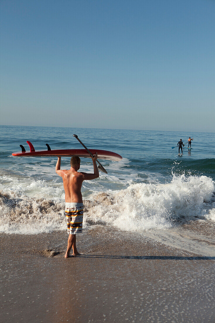 USA, California, Malibu, a paddleboarder watches his friends paddle out at Zuma Beach