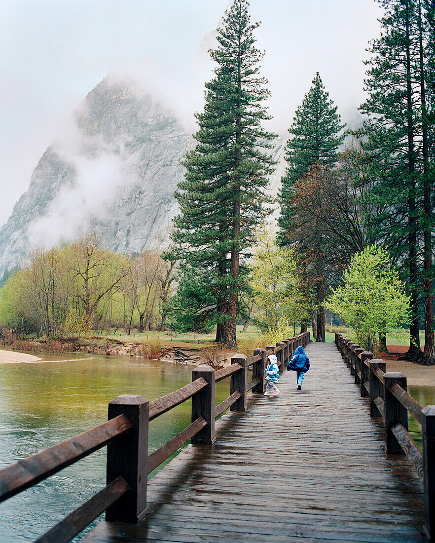 USA, California, Yosemite National Park, kids run across a bridge over the Merced River near Curry Village