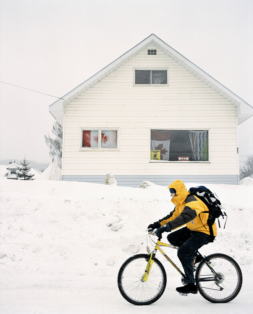 CANADA, man riding bicycle in snow in front of house, Fernie