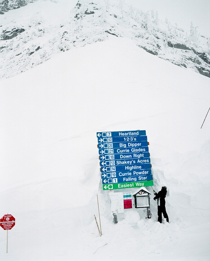 CANADA, person standing shoveling snow from around sign, Fernie Ski Area