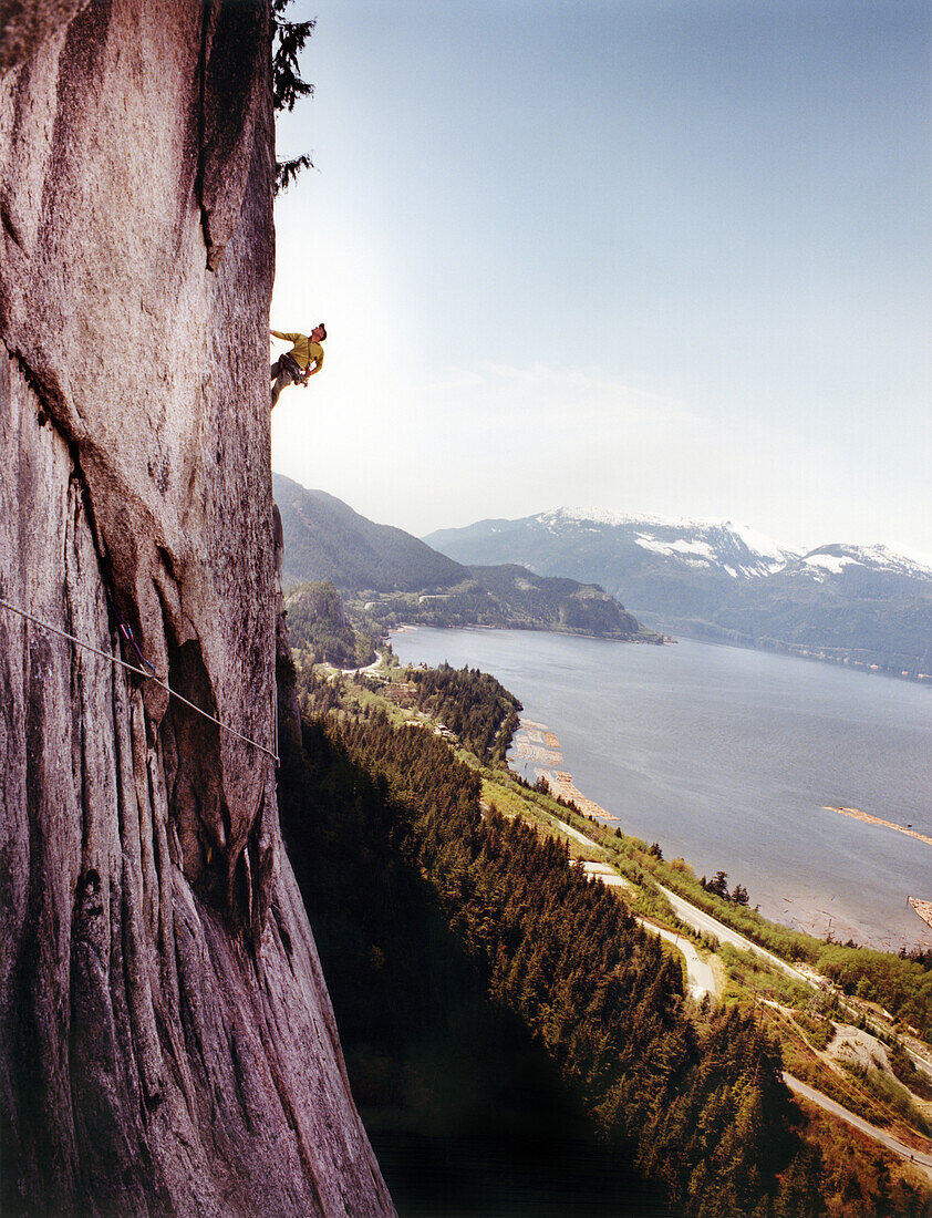 CANADA, man climbing the Stawamus Chief with the Howe Sound in the distance, Squamish, BC