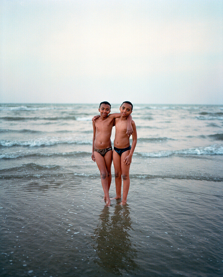 ERITREA, Hamasien, portrait of Eritrean twins standing on the edge of the Red Sea