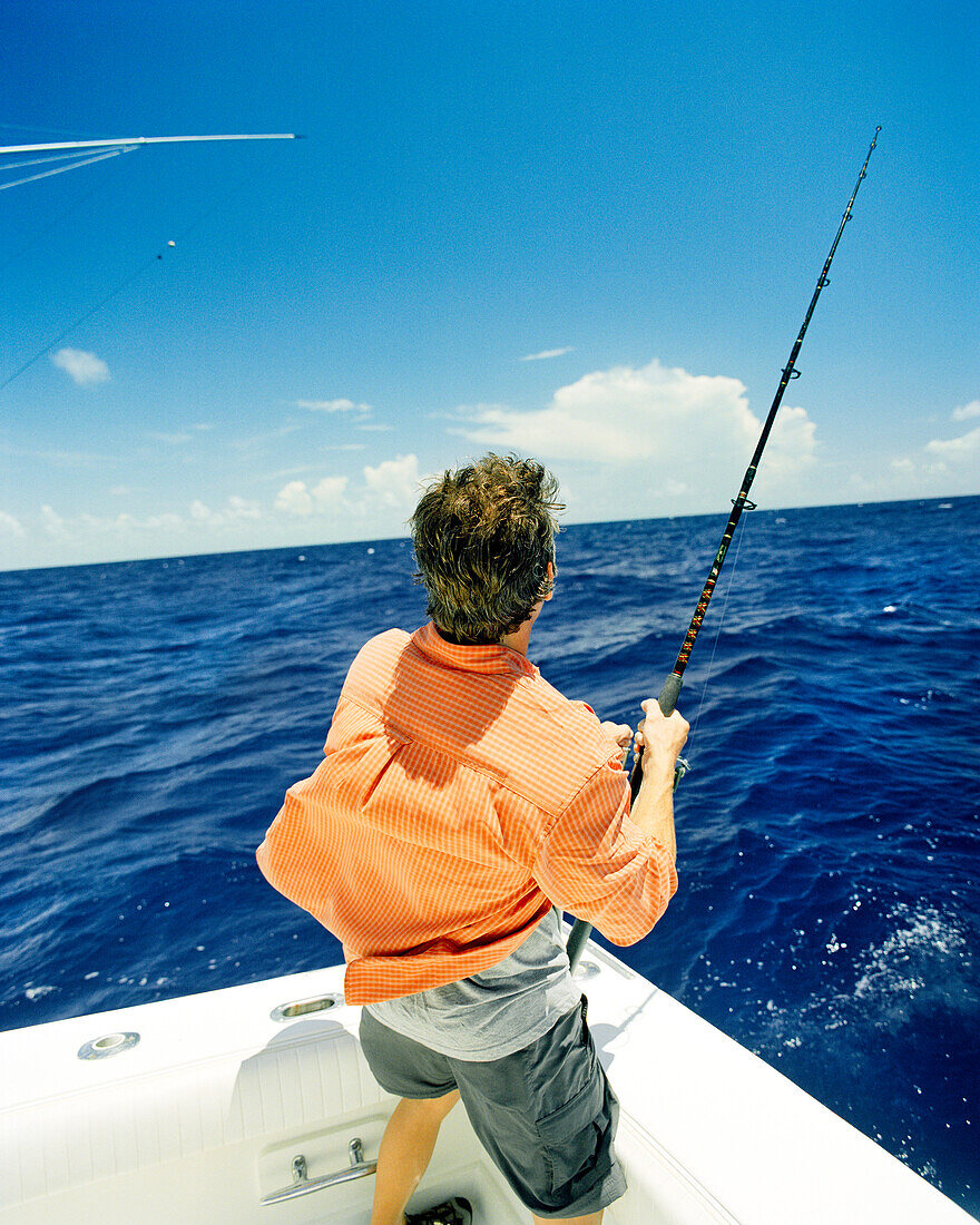 USA, Florida, man reeling in a fish at sea, rear view, Islamorada
