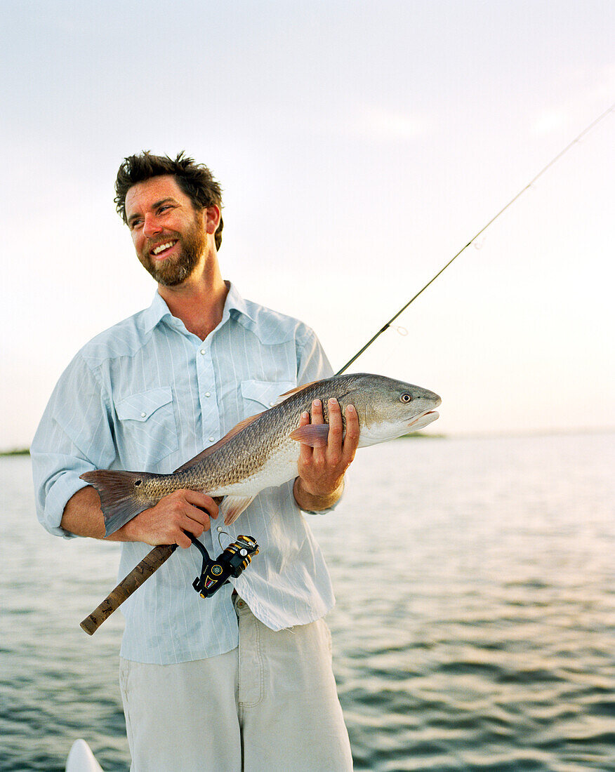 USA, Florida, fisherman holding fishing rod and Redfish, smiling, New Smyrna Beach