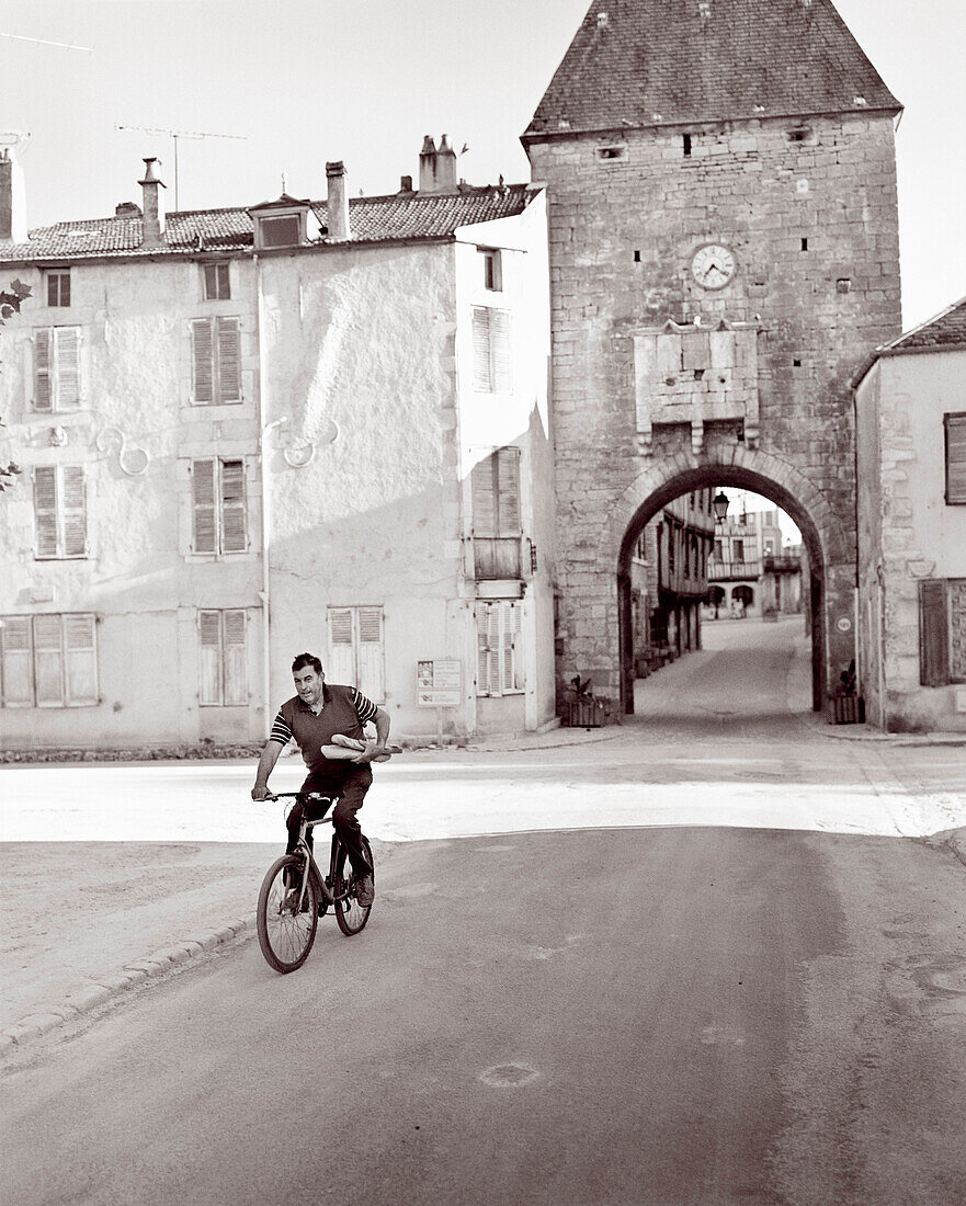 FRANCE, Burgundy, man riding bicycle carrying bread in old town, Noyers (B&W)