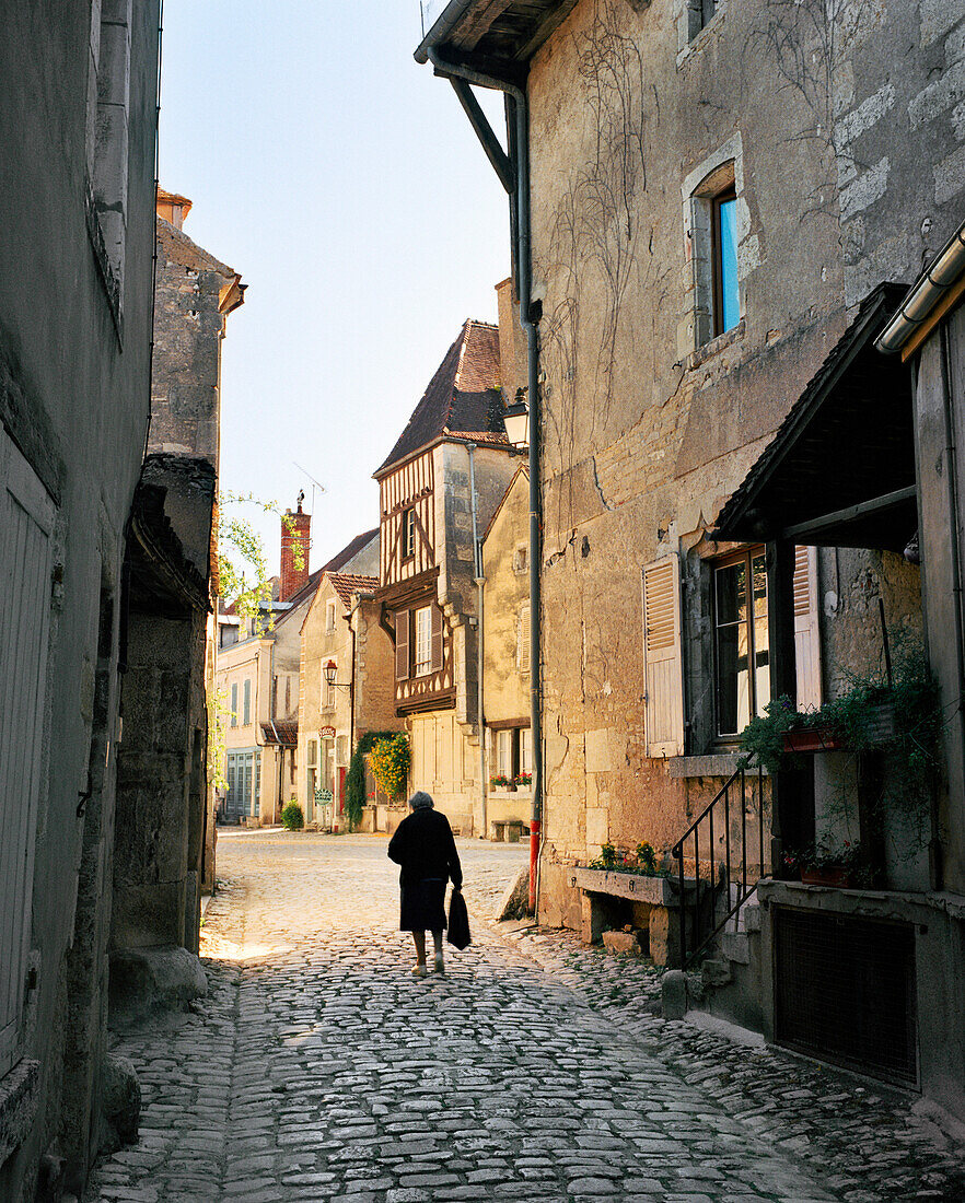 FRANCE, Burgundy, senior woman walking on pathway by buildings, rear view, Noyers