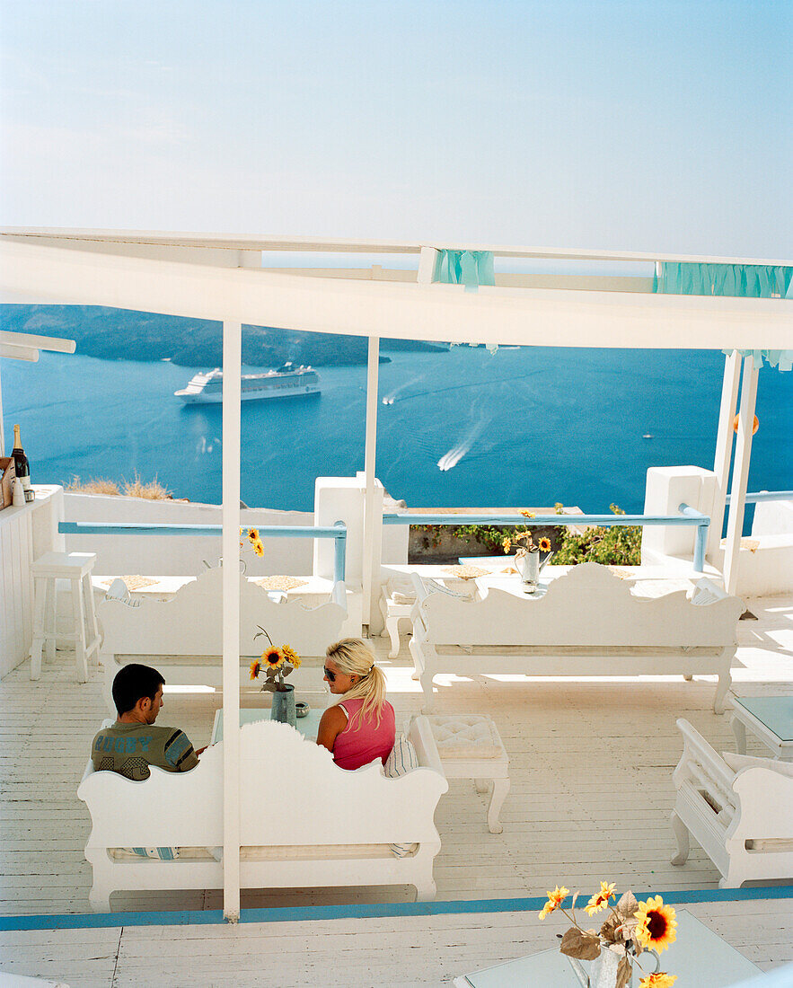 GREECE, Santorini, Fira, a young couple enjoys a drink and shade high above the Mediterranean Sea on the island of Santorini