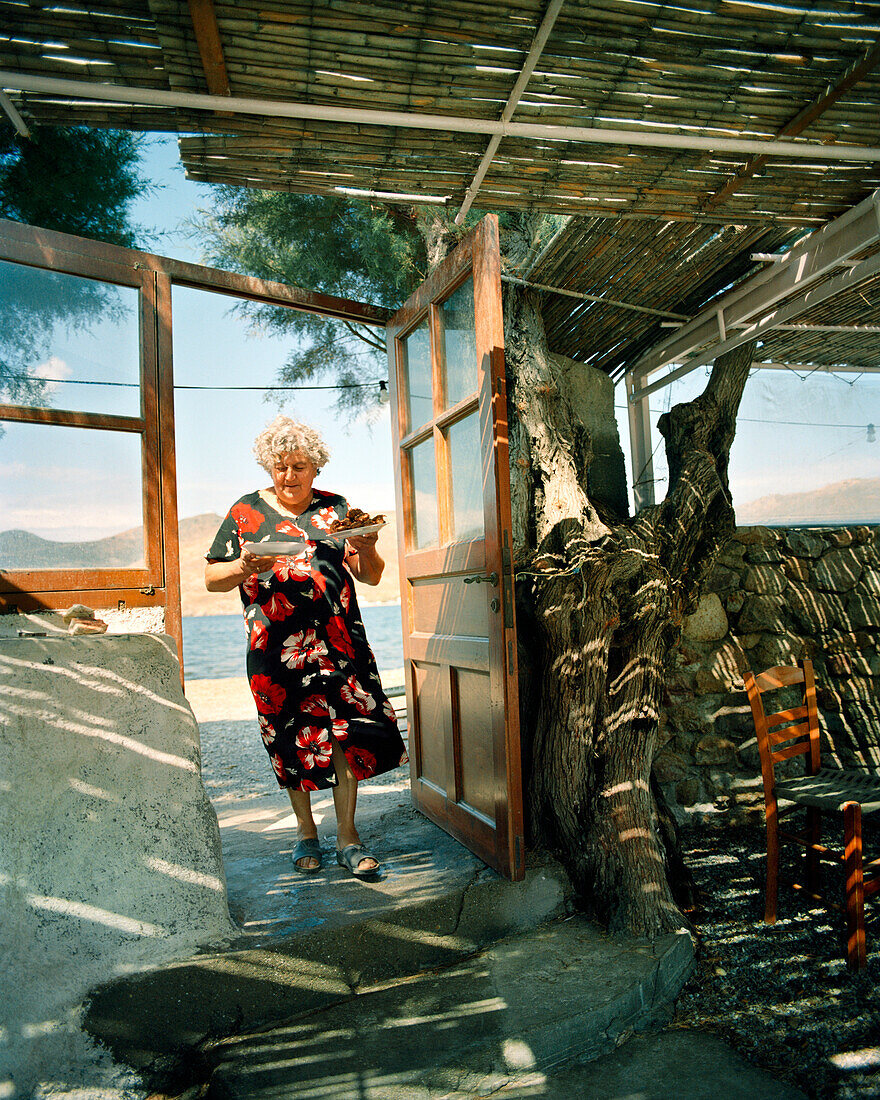 GREECE, Patmos, Diakofti, Dodecanese Island, Katerina Grillakis delivers food to a table at her Diakofti Taverna