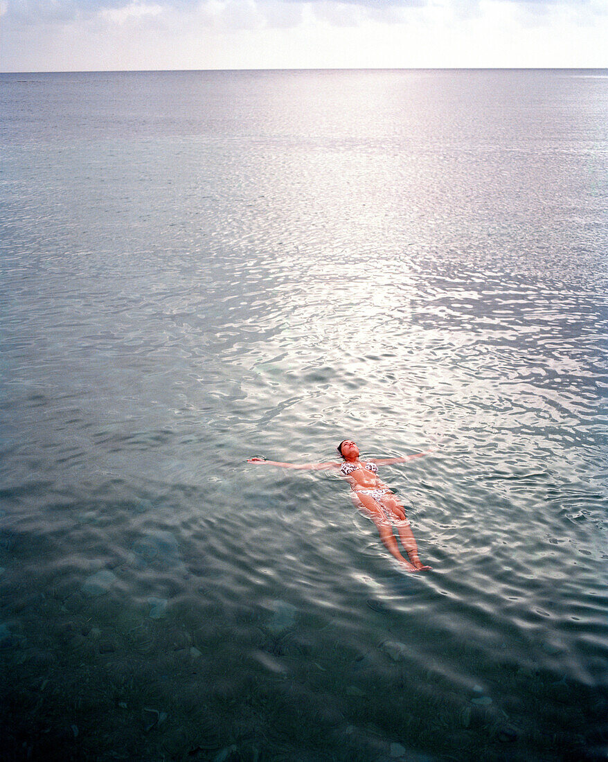 HONDURAS, Roatan, young woman floating in the Caribbean Sea