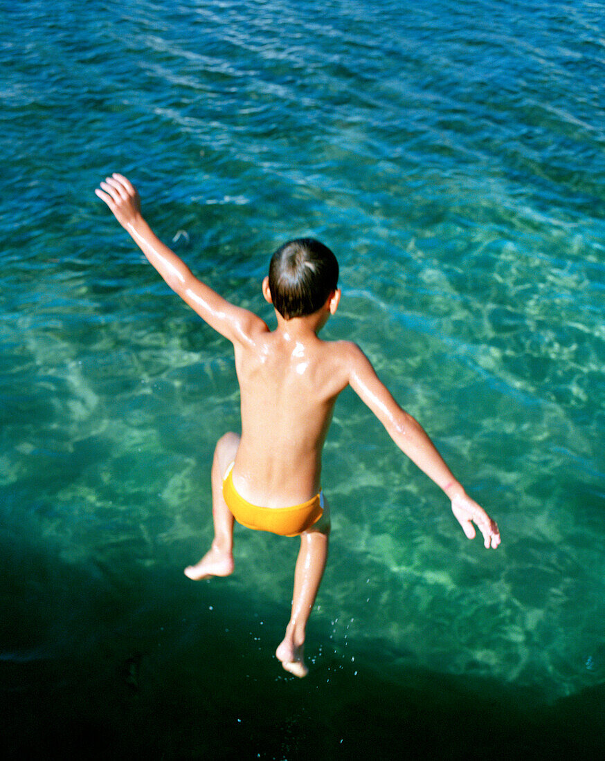 HONDURAS, Roatan, boy jumping into the Caribbean Sea