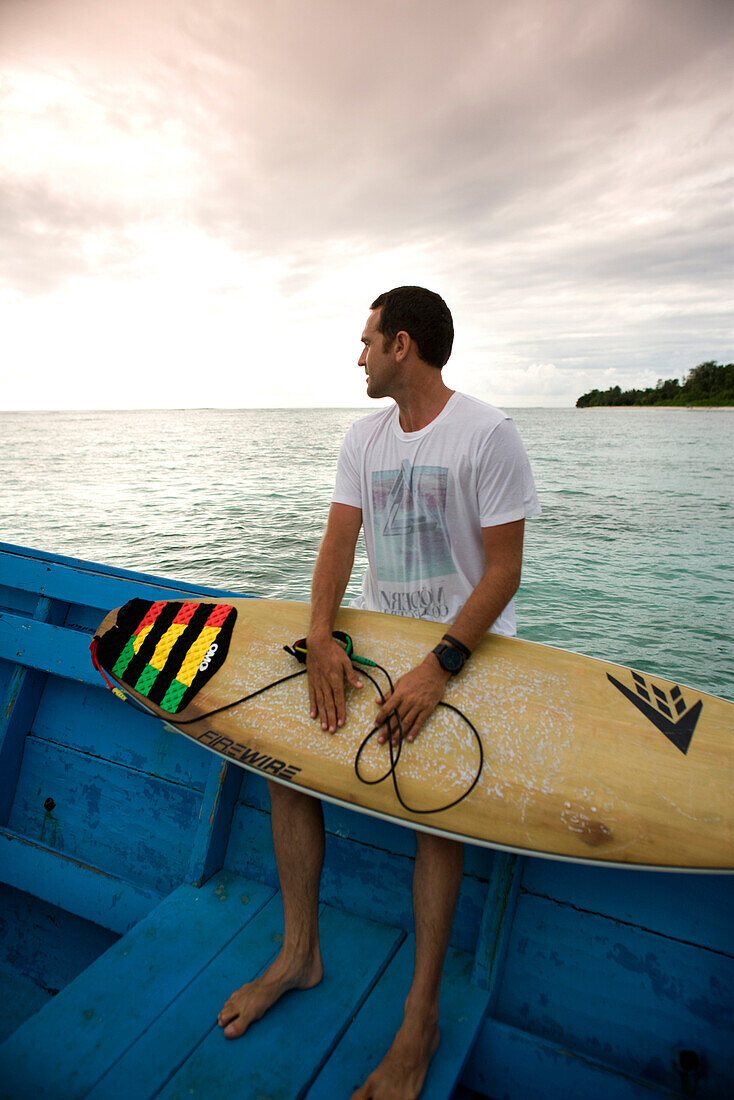 INDONESIA, Mentawai Islands, Kandui Surf Resort, young man sitting on boat with surfboard
