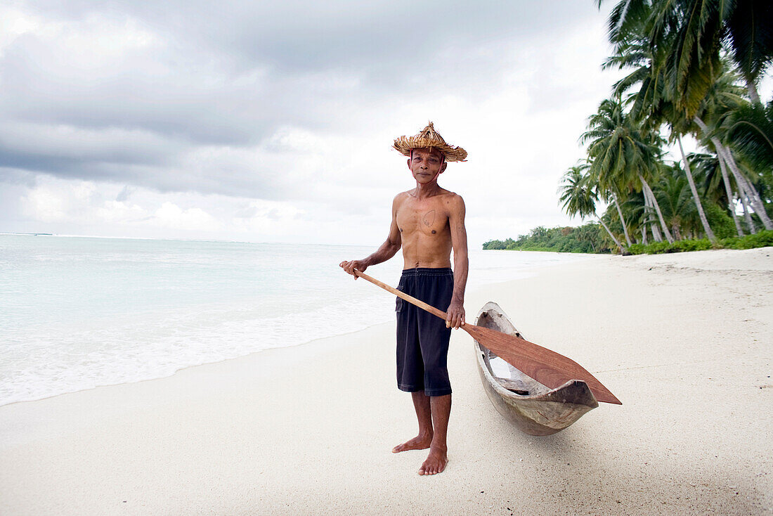 Indonesia, portrait of senior man holding oar by canoe at beach