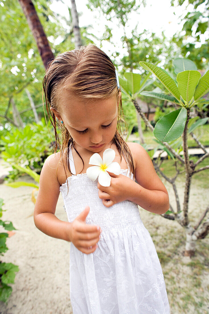 INDONESIA, Mentawai Islands, Kandui Resort, young girl holding a plumeria flower, looking down