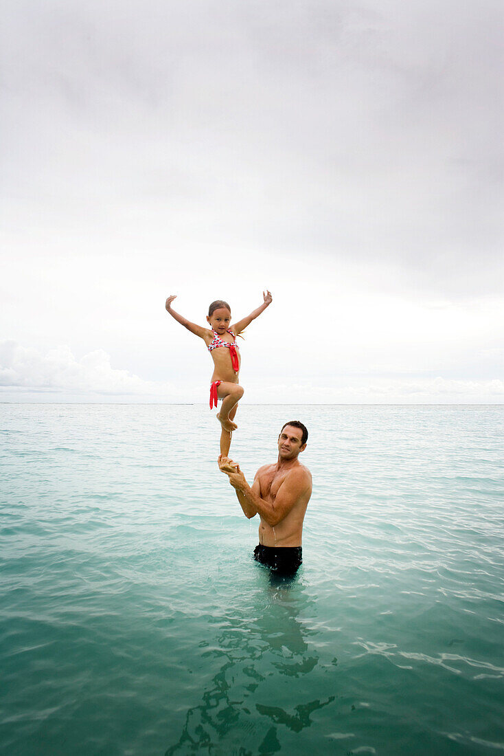 INDONESIA, Mentawai Islands, Kandui Resort, portrait of girl standing on his father's hands in the ocean