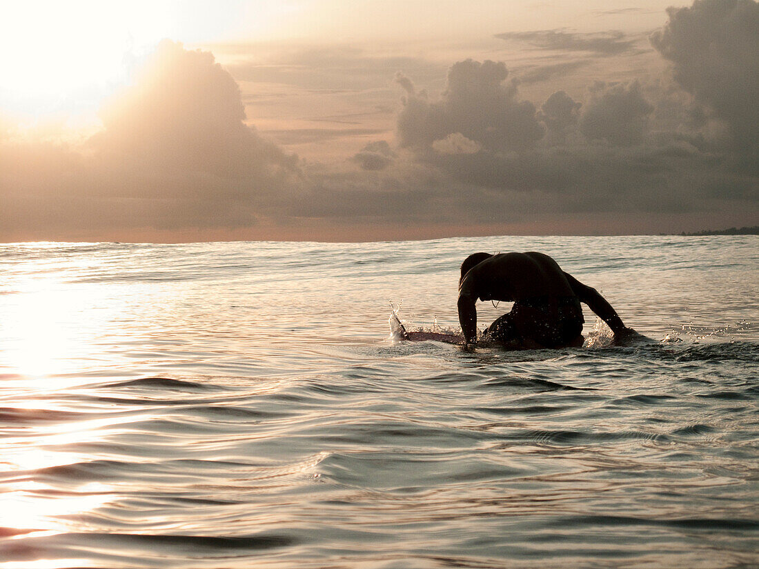 INDONESIA, Mentawai Islands, silhouette of man a man knee paddling his surfboard, Beng Beng