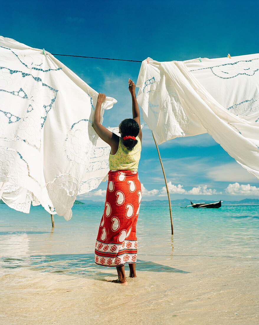 MADAGASCAR, woman hanging tapestries at Jardin Vanille Beach, Nosy Be