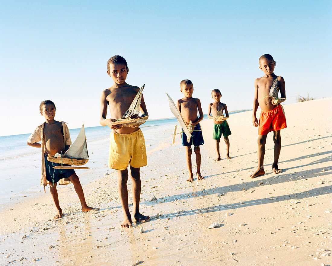 MADAGASCAR, boys holding toy handmade boats at beach, Anjajavy