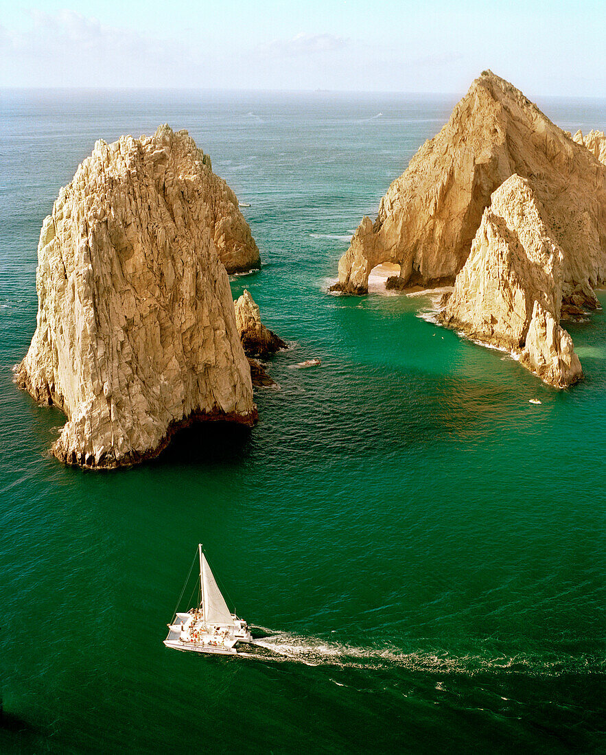 MEXICO, Cabo San Lucas, Baja, a catamaran sailing by the archway at Lover's Beach, also known as Land's End