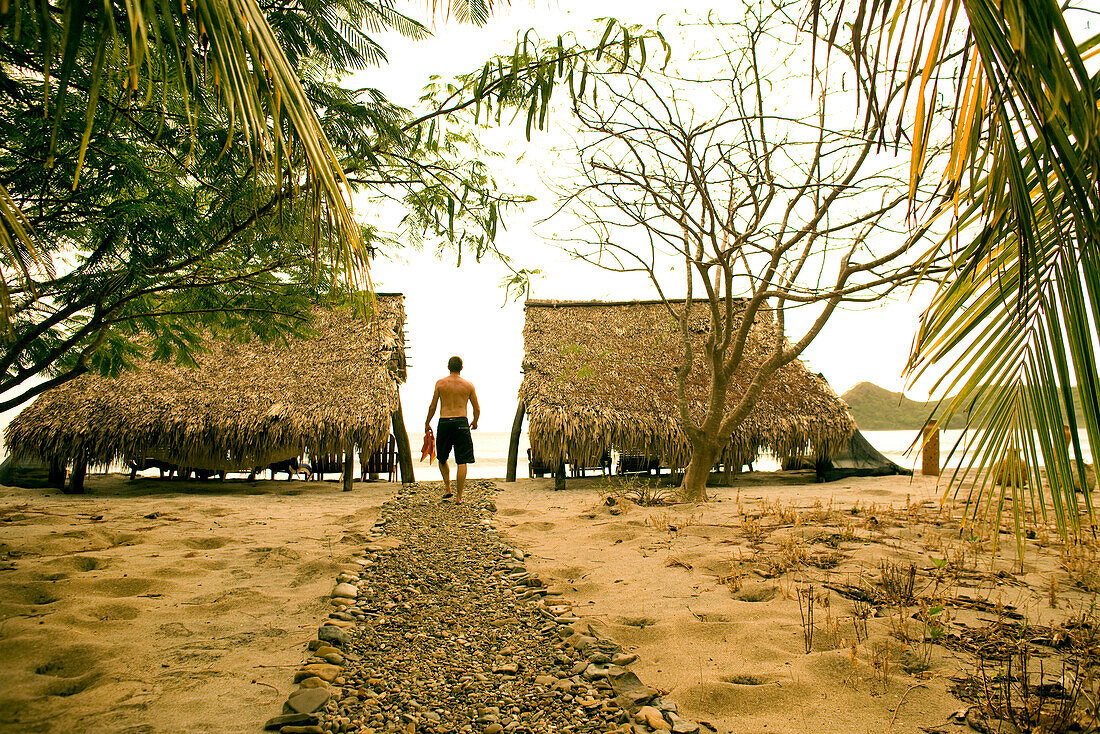 NICARAGUA, San Juan Del Sur, a man walks to the beach with his fins at Morgan's Rock Lodge, Morgan's Rock