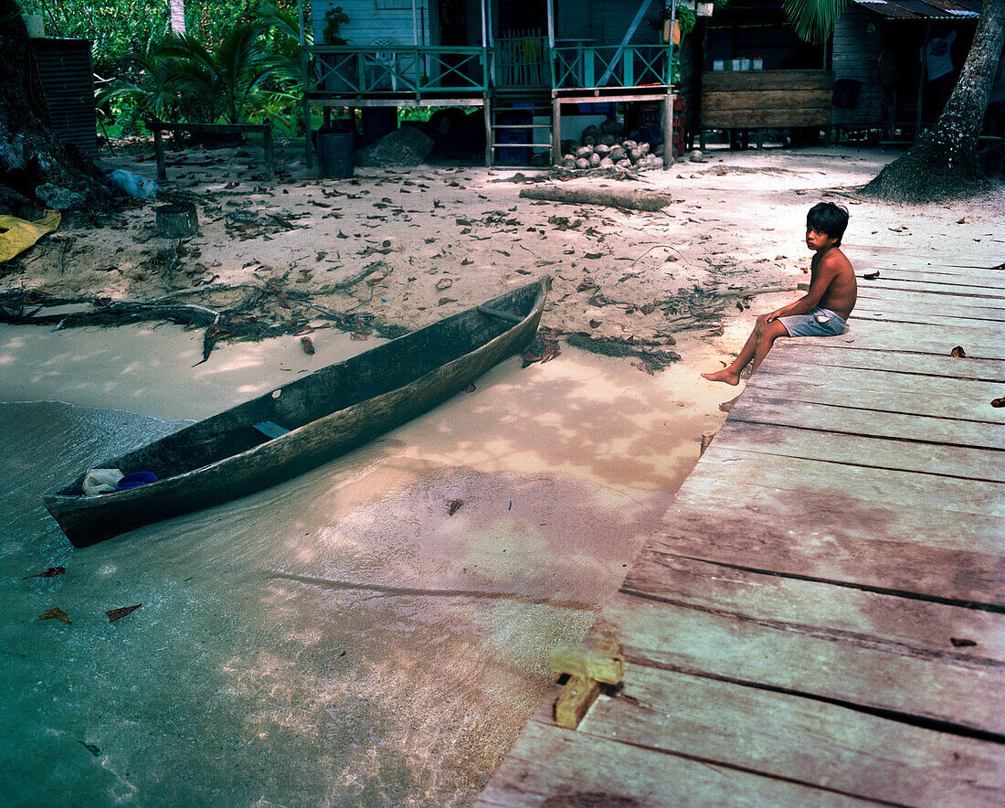 PANAMA, Bocas del Toro, Salt Creek Islands, Guaymi Indian boy sits on a dock by a dugout canoe, Central America