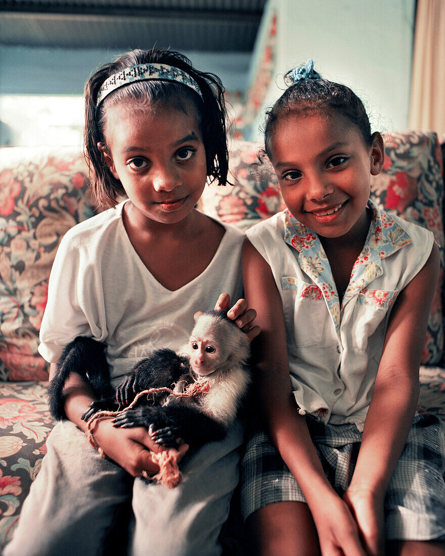 PANAMA, Bocas del Toro, portrait young girls hold a pet monkey in their home, Central America