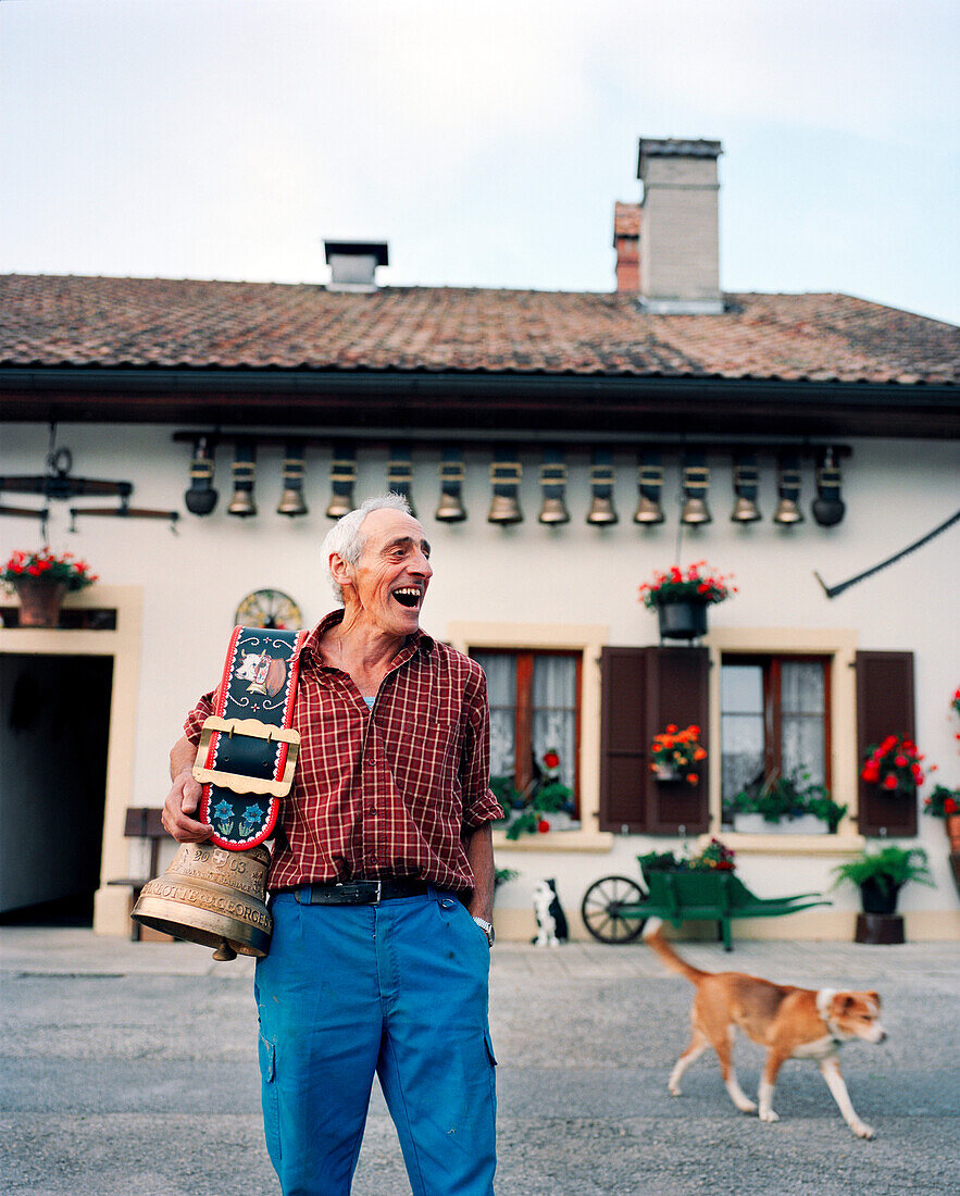 SWITZERLAND, Motiers, George Montandon stands in front of his home holding a cow bell that was given to him by a friend for his 45th wedding anniversary, Jura Region