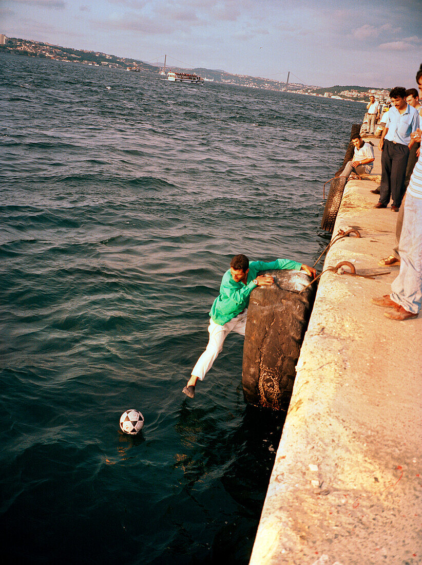 TURKEY, Istanbul, a man tries to reach out from a pier to retrieve his soccer ball, the Sea of Marmara