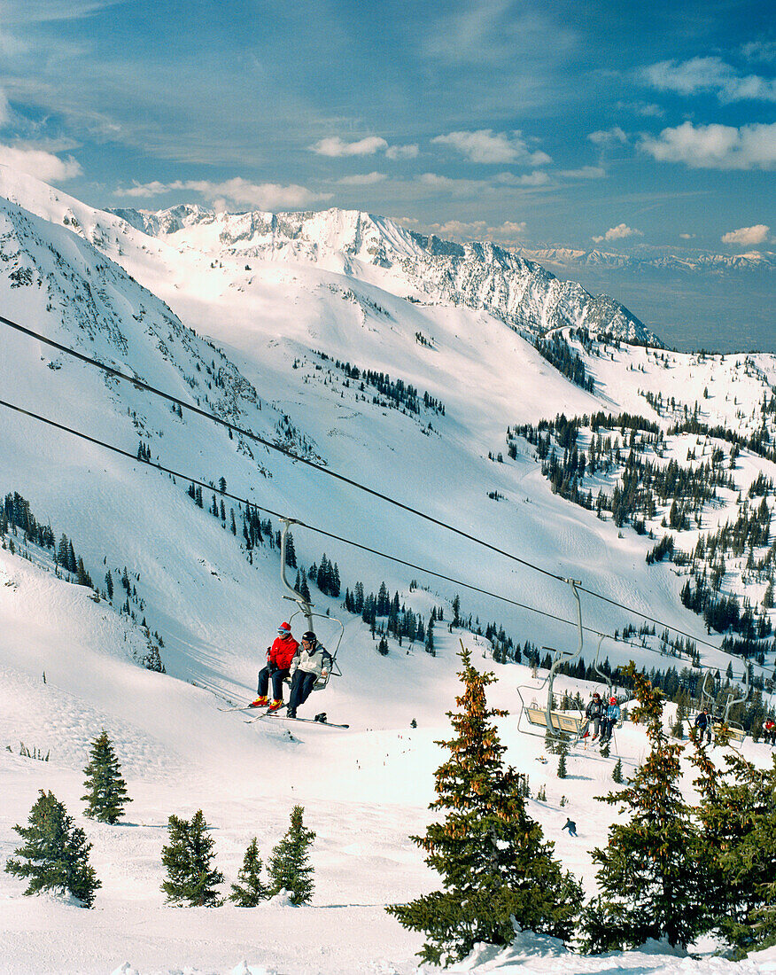 USA, Utah, friends sitting on Little Cloud Ski Lift with views to Salt Lake City, Snowbird Ski Resort