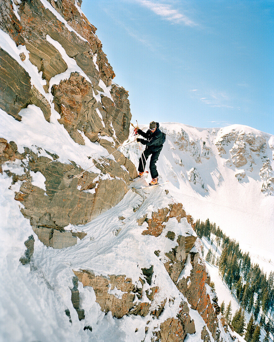 USA, Utah, skier climbing around rocky cliff, holding onto a rope, High Sunspot, Alta Ski Resort