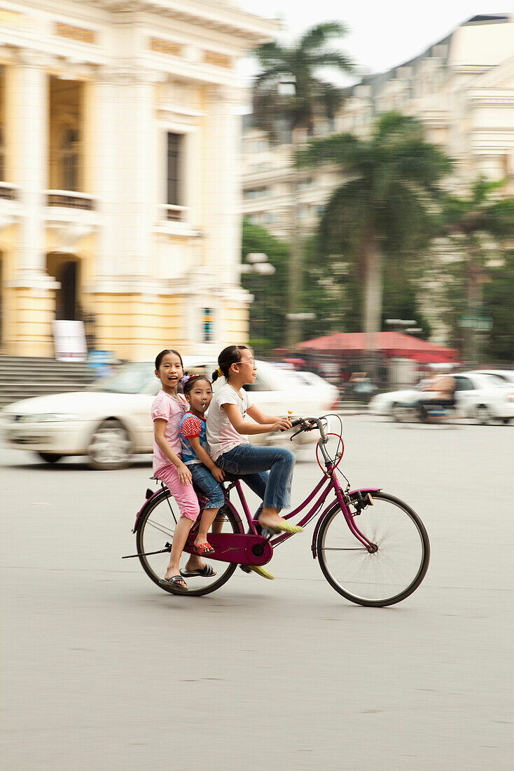 VIETNAM, Hanoi, three young girls ride through the center of town