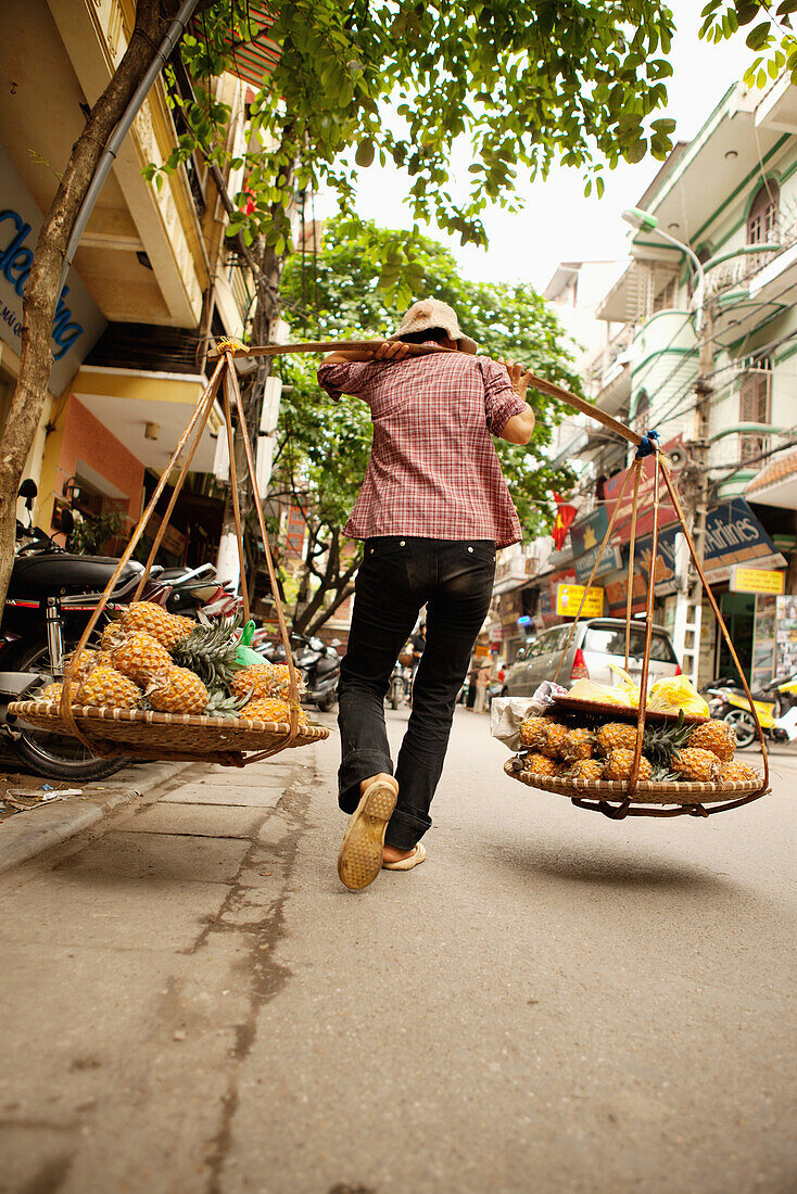 VIETNAM, Hanoi, a street scene of a woman walking down the street selling pineapples