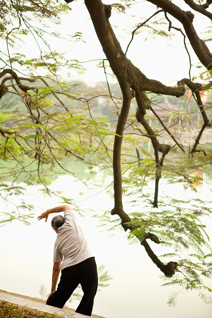 VIETNAM, Hanoi, a woman performs Tai Chi and stretches early in the morning, Hoan Kiem Lake