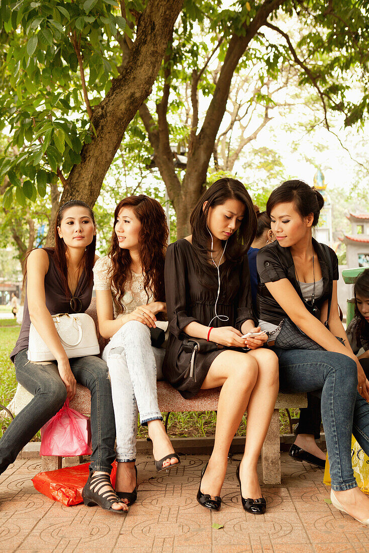 VIETNAM, Hanoi, young women sitting together on a bench by Hoan Kiem Lake
