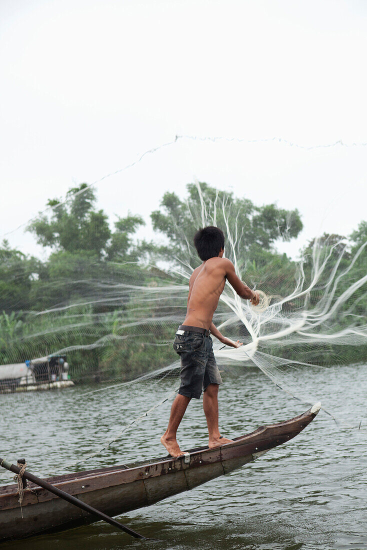 VIETNAM, Hue, Perfume river, fisherman Tran Van Son casting his fishing net from the bow of his Sampan boat, La Y Village, Phu Vang District, Thua Thien Hue Province