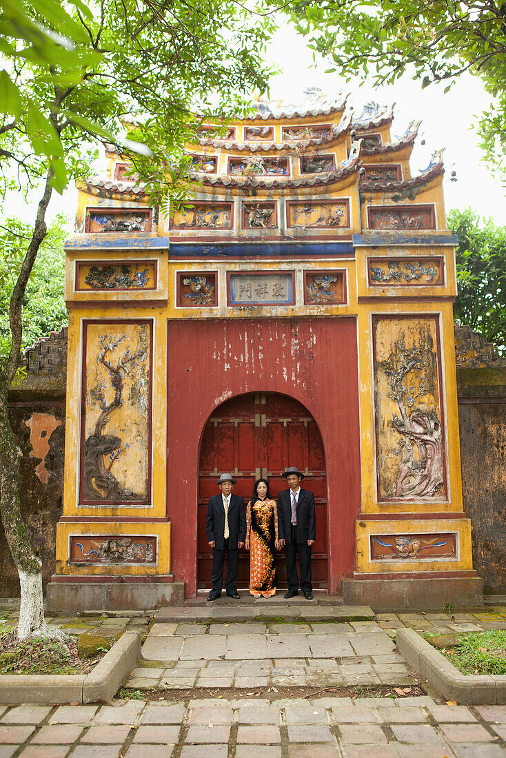 VIETNAM, Hue, a woman stands with her husband and brother in law by a large painted gate in the Citadel