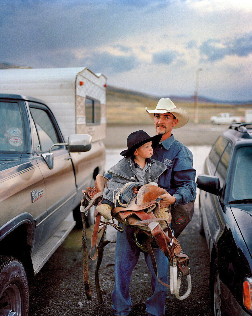 USA, Wyoming, portrait of Saddle Bronc Cowboy carrying his son and saddle, Cody Rodeo