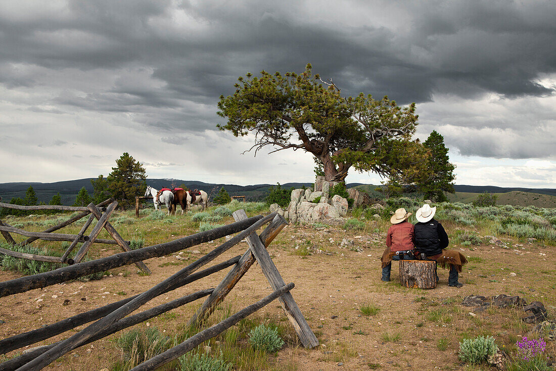 USA, Wyoming, Encampment, two women wranglers sit on a log at the top of a mountain, Abara Ranch