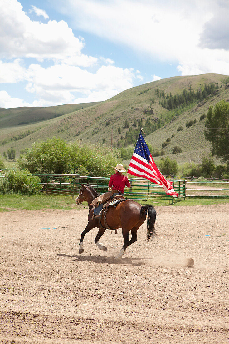 USA, Wyoming, Encampment, a young man rides his horse carrying the American flag, Abara Ranch