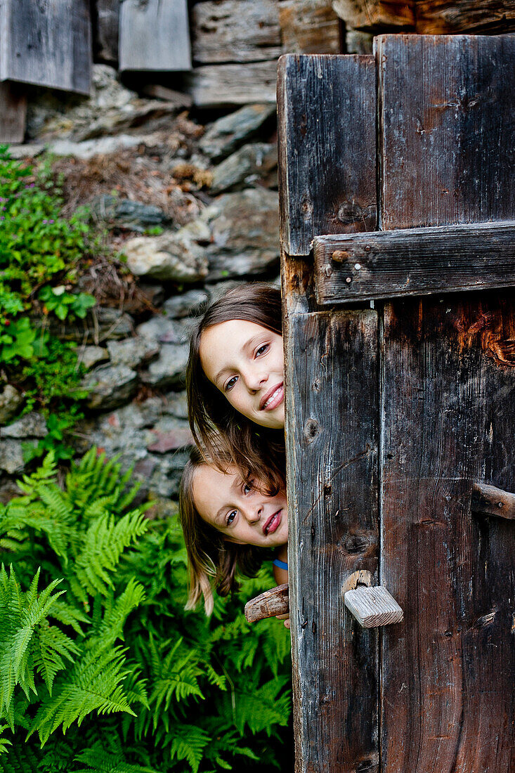 Zwei Mädchen hinter einer alten Holztür, Steiermark, Österreich