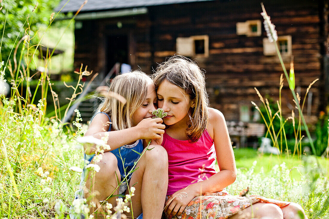 Zwei Mädchen riechen an einer Blume, Steiermark, Österreich