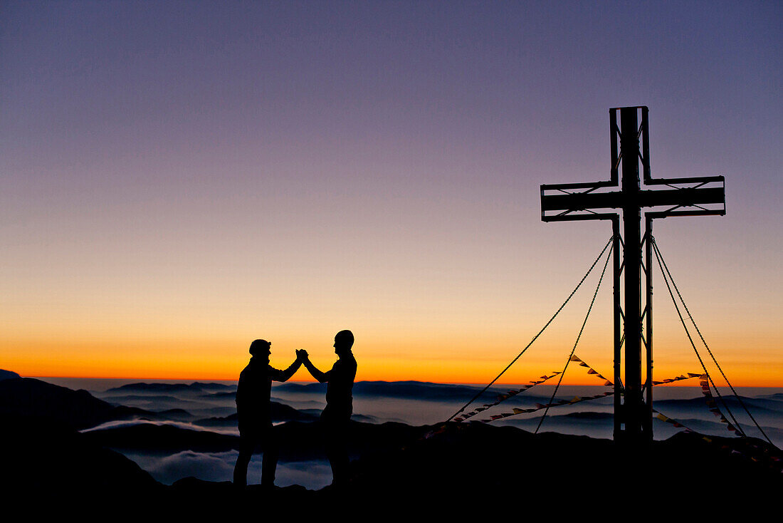 Two hikers at summit of Hochschwab mountain at sunrise, Hochschwab, Styria, Austria