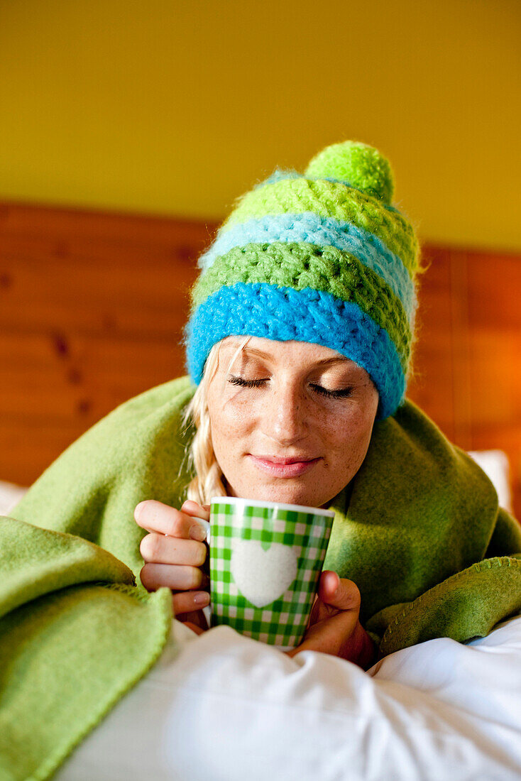 Young woman wearing a wolly hat lying in a bed, Fladnitz an der Teichalm, Styria, Austria