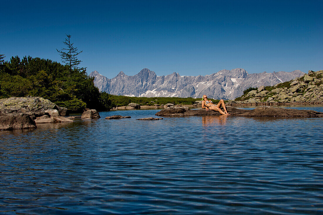 Woman sunbathing at lake Spiegelsee, Dachstein mountains in background, Styria, Austria