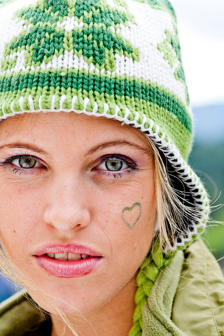 Junge Frau mit Mütze und Herzen auf der Wange, Steiermark, Österreich